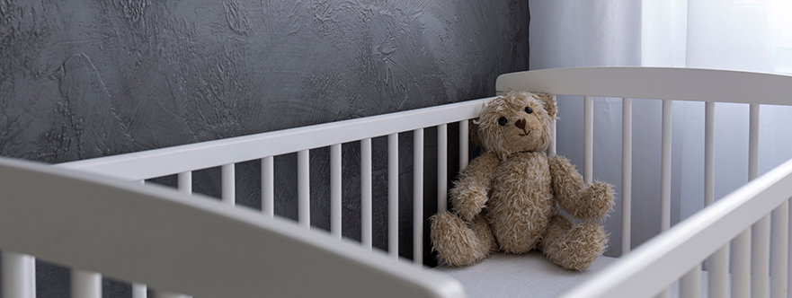 Empty crib with a teddy bear in a gray room