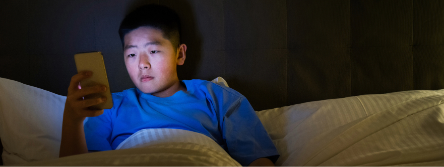 Teen boy looking at smartphone in bed