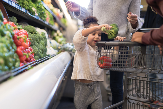 young child putting produce in shopping cart