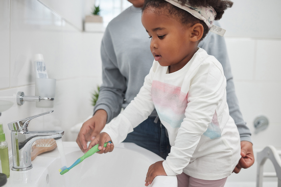 Young girl holding her toothbrush under the faucet