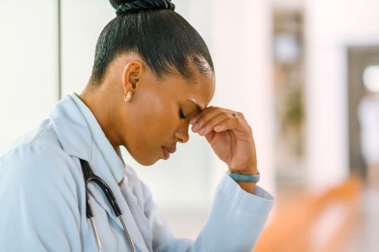 A healthcare professional in a white coat sits with a thoughtful expression.