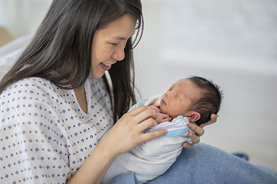 Woman in hospital gown holding newborn baby.
