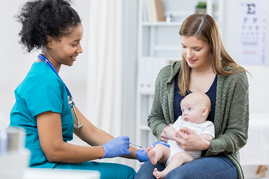 Baby getting vaccine in thigh while sitting on mother's lap.